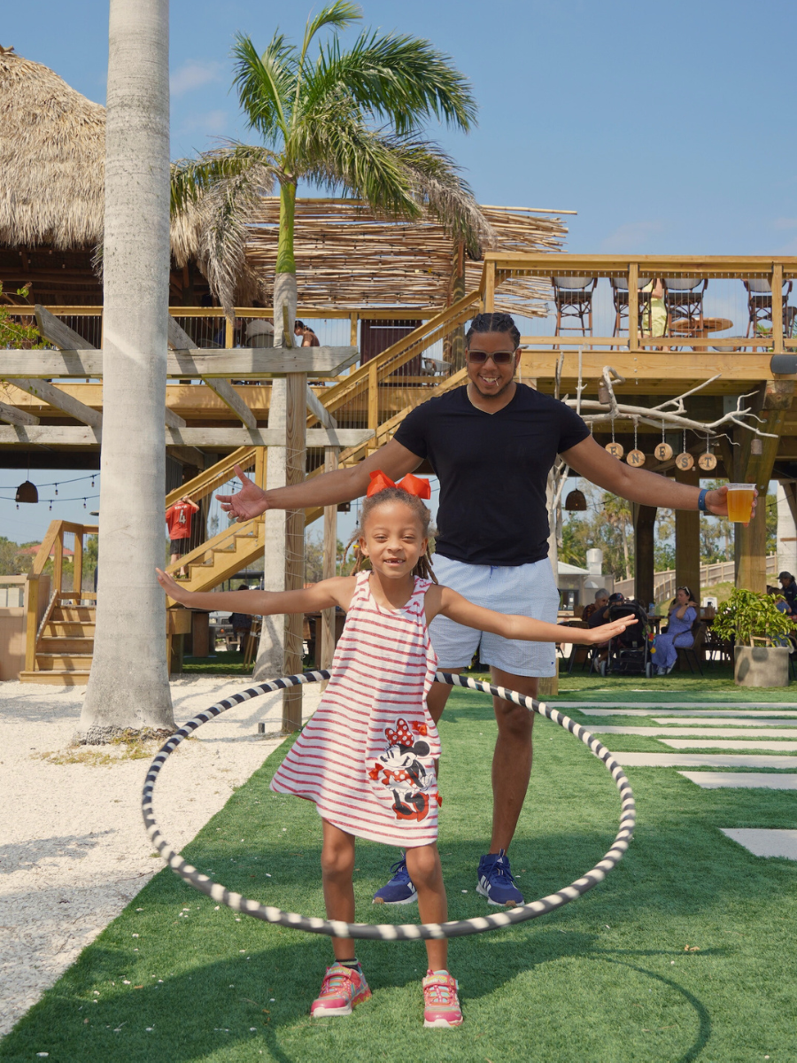 Little girl hulahoops while her dad celebrates behind her